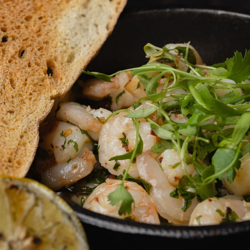 Close-up of shrimp scampi with fresh herbs, toasted bread, and a grilled lemon slice.