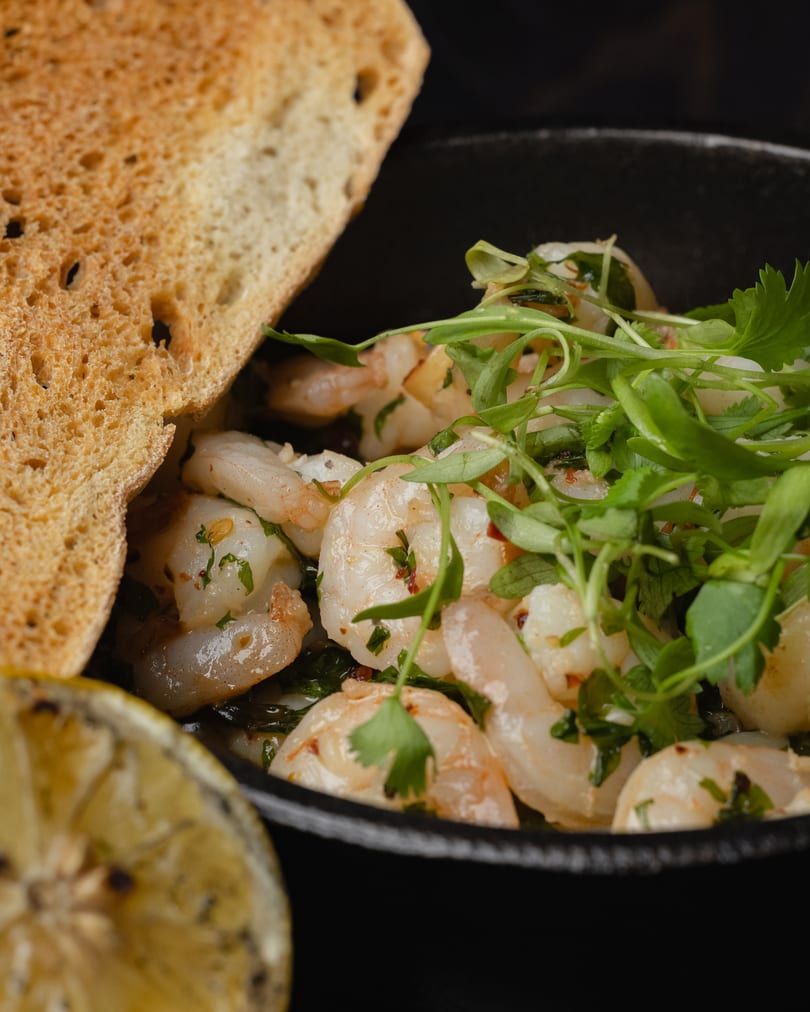 Close-up of shrimp scampi with fresh herbs, toasted bread, and a grilled lemon slice.