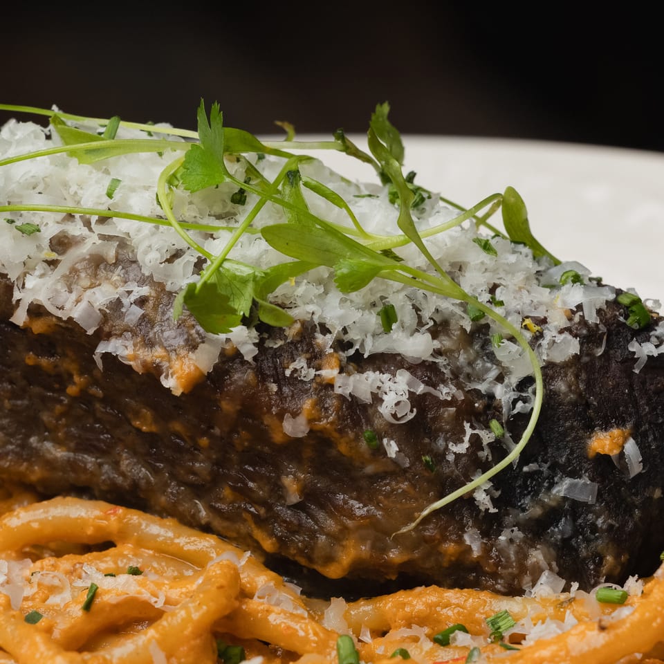 Braised short rib with grated cheese and herbs, served over pasta with a creamy orange sauce.