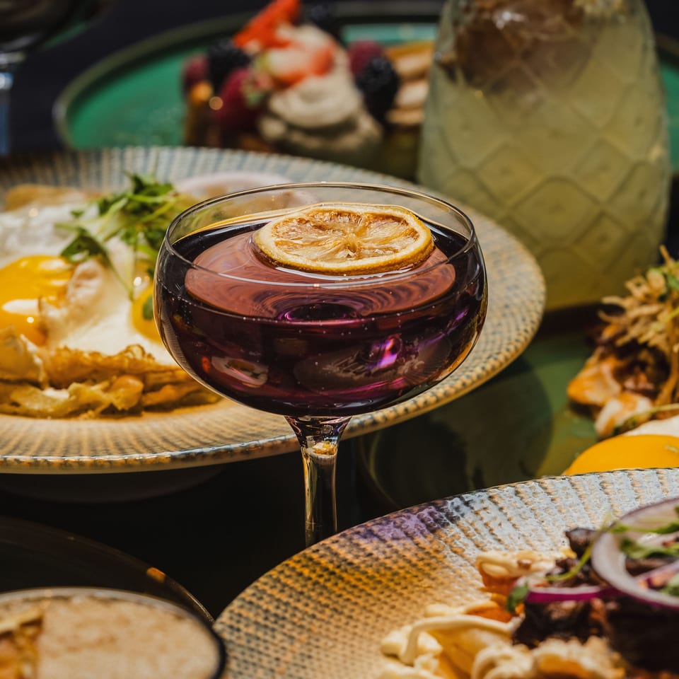 A vibrant table spread with a purple cocktail, fried eggs, and other dishes.