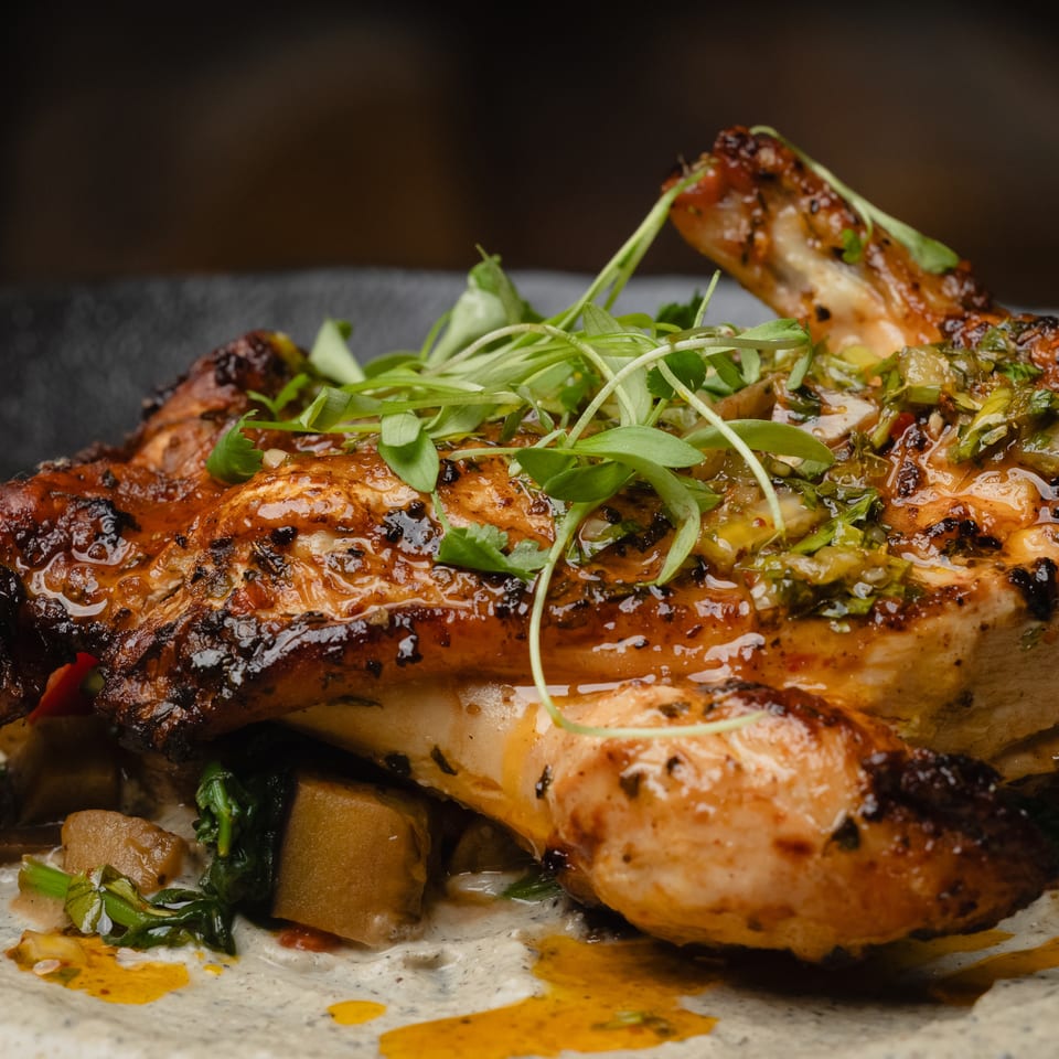 Roasted chicken with crispy skin, topped with fresh herbs and sauce, served on a bed of vegetables.