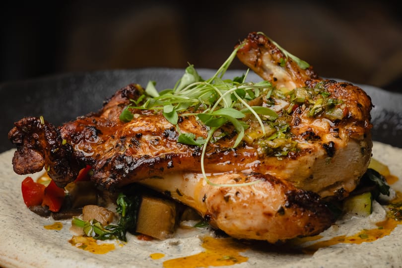 Roasted chicken with crispy skin, topped with fresh herbs and sauce, served on a bed of vegetables.