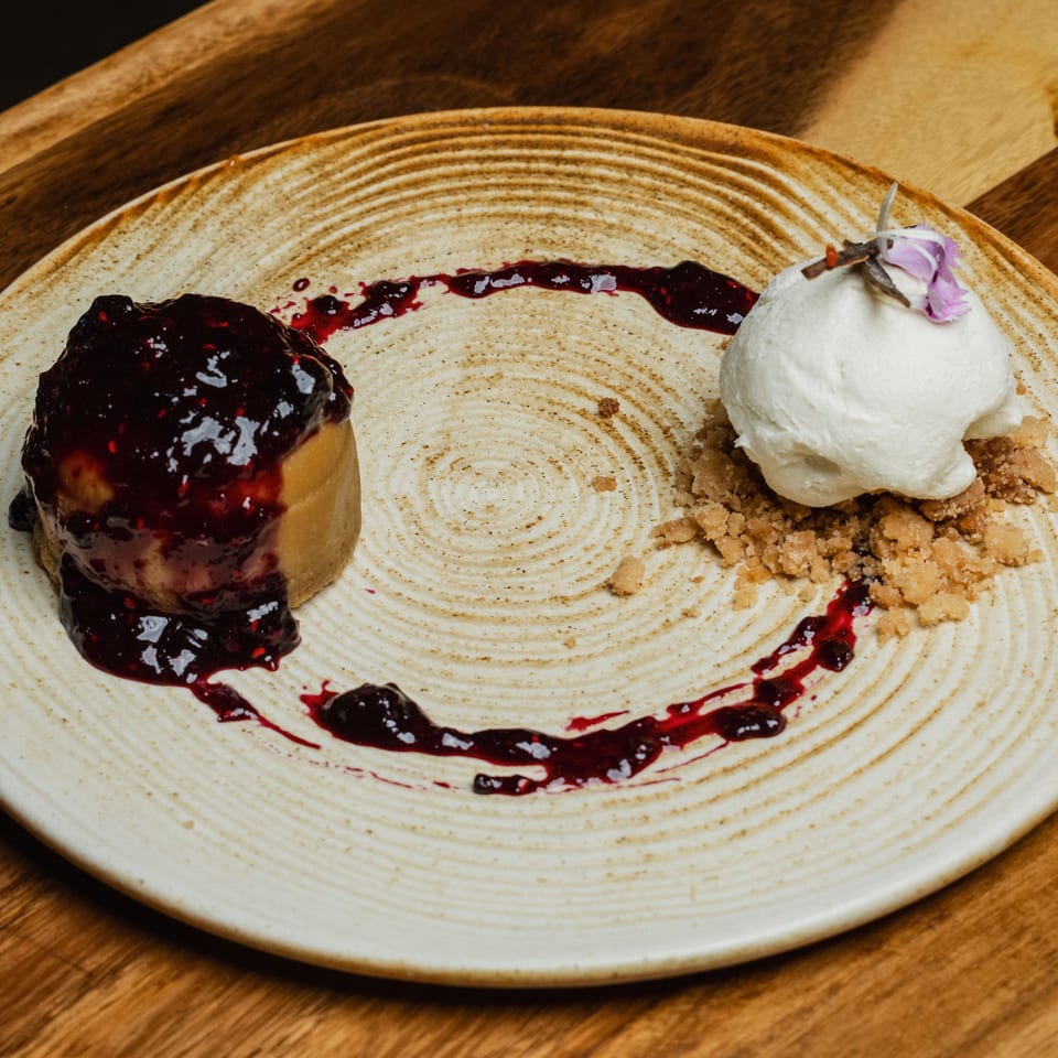 A dessert with berry compote, a scoop of ice cream, and crumble on a textured plate.