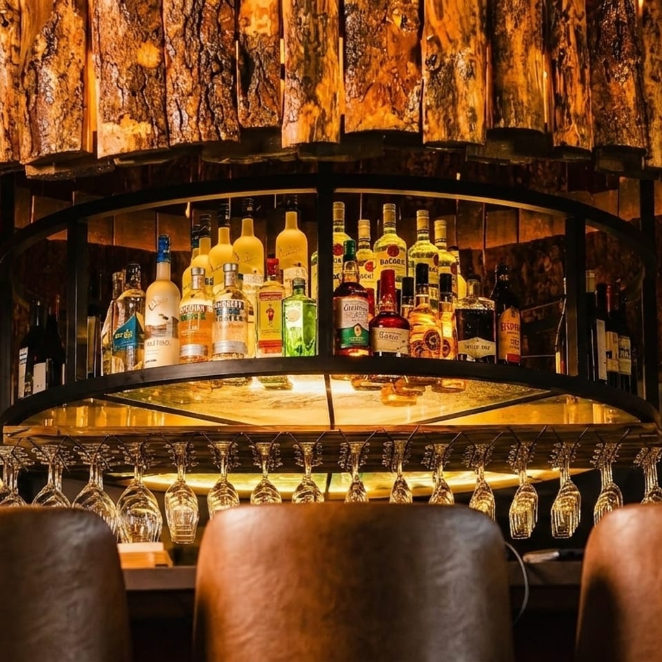 A rustic bar with a wooden chandelier, liquor bottles, hanging glasses, and bar stools.