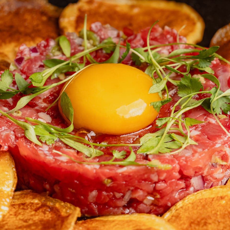 Beef tartare with a raw egg yolk and microgreens, surrounded by toasted bread slices.