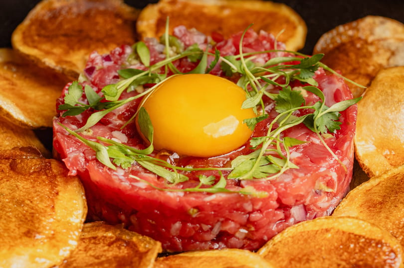 Beef tartare with a raw egg yolk and microgreens, surrounded by toasted bread slices.
